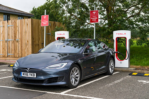 Abington, Scotland, UK - August 7, 2016: A Tesla electric car parked at a Tesla super charger charging station in the car park of Abington services in Lanarkshire, Scotland. The car is plugged into the super charger.