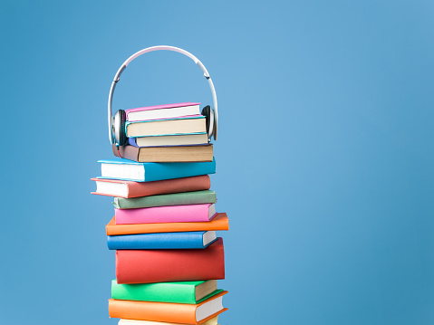 Headphones on top of stack of multicolored hardcover books.The background is blue and headphones are placed over books.Shot in studio with medium format camera Hasselblad.Nobody is seen in photo.