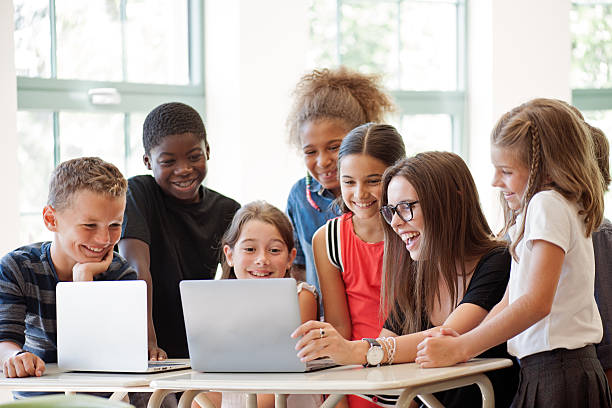 school children usando computadora portátil con el profesor en un aula - elementary student child laughing group of people fotografías e imágenes de stock