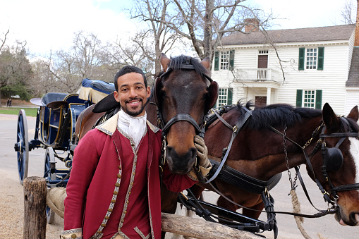 Williamsburg, Va. USA - April 9, 2016: A Colonial Williamsburg reenactor shows his horse some affection before heading out in the toursist destination to gvie tourist their carriage ride through the historic city.