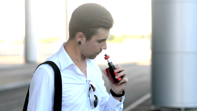 Young man smoking electronic cigarette at city