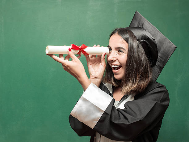 istock Young Graduate Woman Looking Through Her Diploma As A Binocular 586350622