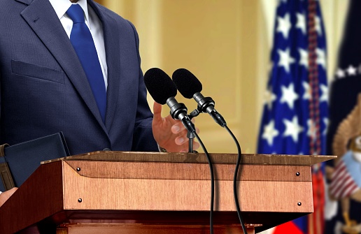 USA politician giving a speech on a podium and smiling with flag in the background