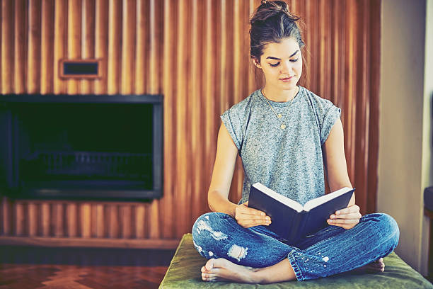 istock Young woman reading book while sitting on ottoman at home 586363464