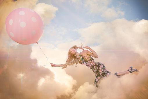 Woman floating mid air in clouds with large pink balloon