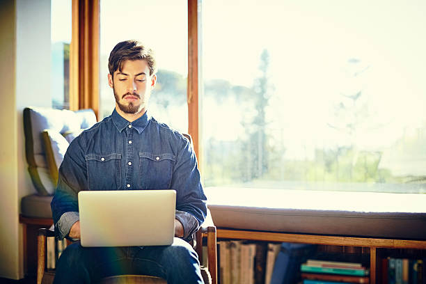 istock Handsome young man using laptop on chair at home 586365092