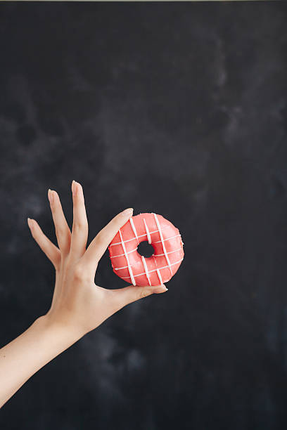 Pink donut in a woman's hand on black background