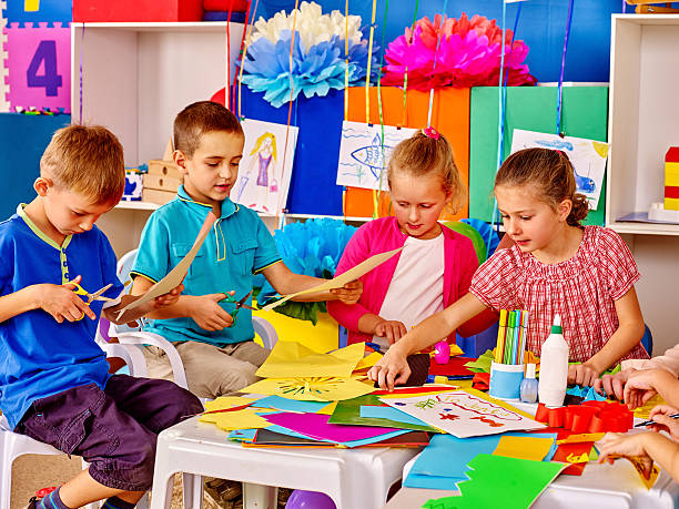 Children with teacher are making something out of colored paper. stock photo