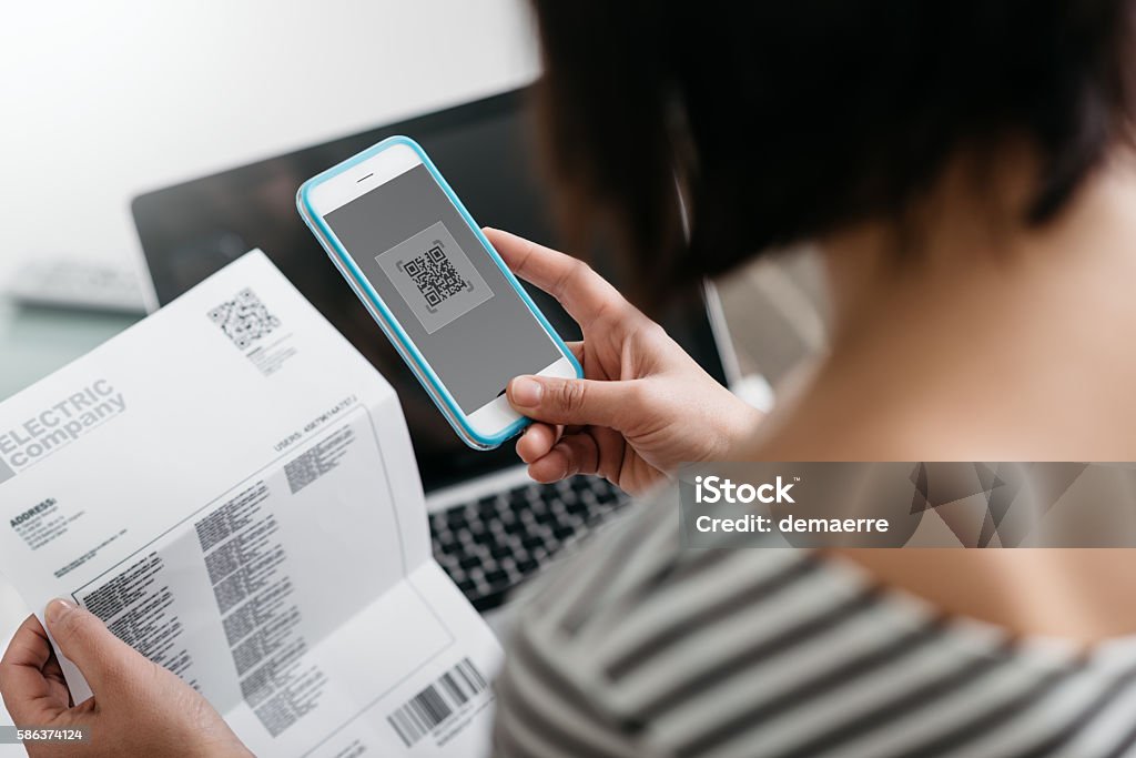 Woman paying bills with her smartphone Woman checking an electricity bill, she is making a contactless payment using her smartphone Financial Bill Stock Photo