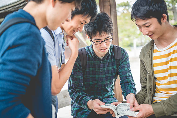 Japanese Students Reading Manga, Chion-ji Temple Park, Kyoto, Japan, Asia Four male Japanese students looking at Manga, having fun in the park of The Chion-ji Temple, Kyoto, Japan, Asia.  Copy space. Nikon D800, full frame, XXXL. iStockalypse Kyoto 2016. reading comic book stock pictures, royalty-free photos & images