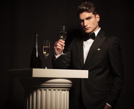 Side view of a elegant young business man holding up a glass of hampagne.