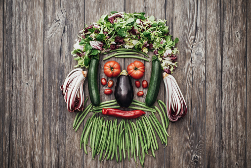 Smiling face of a man with beard made with fresh colorful vegetables on a rustic wooden worktop