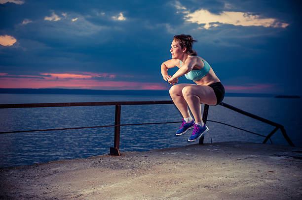 Strong young woman doing plyometric exercises on pier Young strong woman in sportswear doing plyometric exercises on pier. Jump squats, fitness workout outdoors. burpee stock pictures, royalty-free photos & images