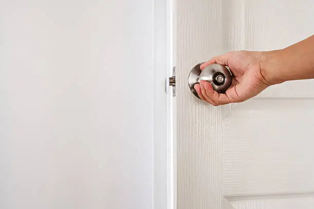 Hand holding door knob, white door and wall, with copy space