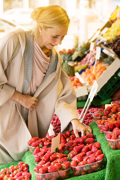 istock woman standing at fruit stand looking at strawberries 586387876