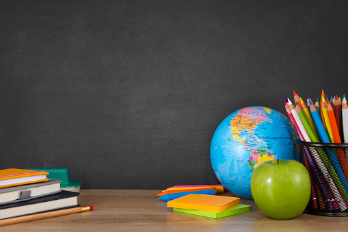 World globe with school supplies on  desk in front of a blackboard.