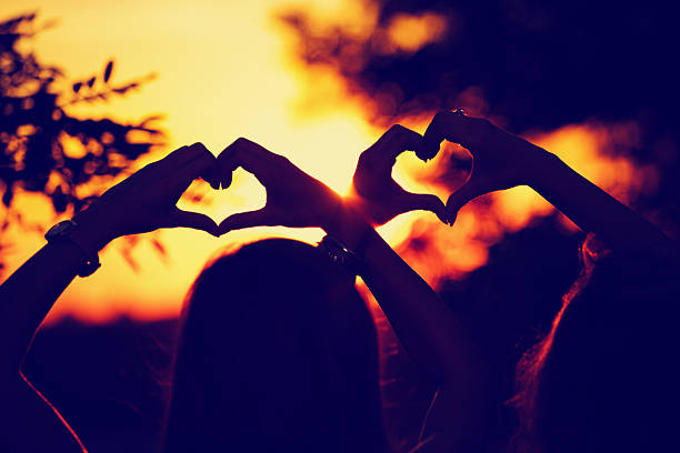 Girl-friends making a heart-shape for the sunset.