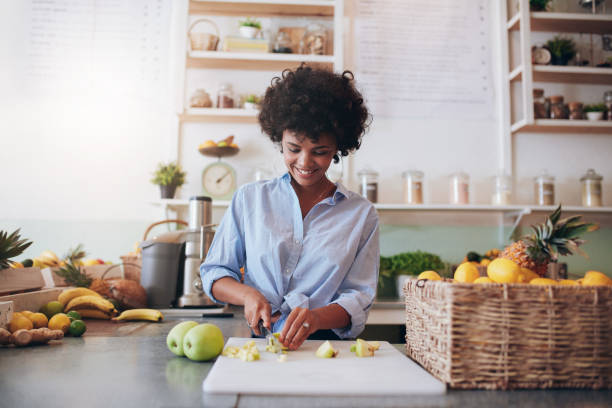 Young woman making fresh juice Indoor shot of attractive young woman chopping fruit to make a fresh juice. African female working at juice bar. juice bar stock pictures, royalty-free photos & images