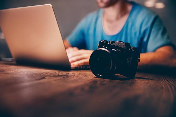 Man doing postproduction of his photos on laptop at night Close-up of vintage looking camera on table with laptop in background editor photos stock pictures, royalty-free photos & images
