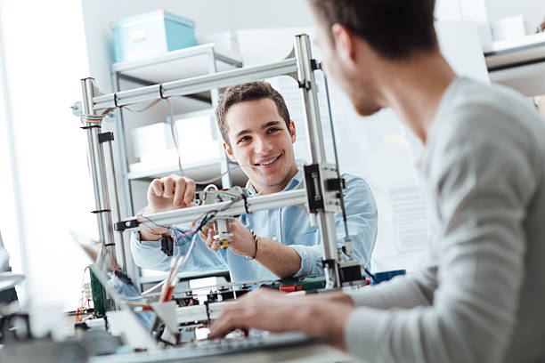Engineering students working in the lab Engineering students working in the lab, a student is adjusting a 3D printer's components, the other one on foreground is using a laptop 3d printing lab stock pictures, royalty-free photos & images