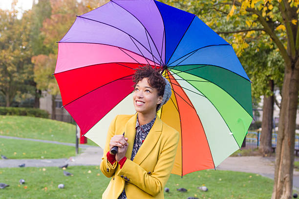istock Young pretty woman under multicolored umbrella in a park 586393498