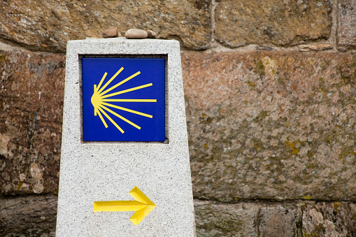 Camino de Santiago milestone, pilgrims scallop symbol, yellow arrow.