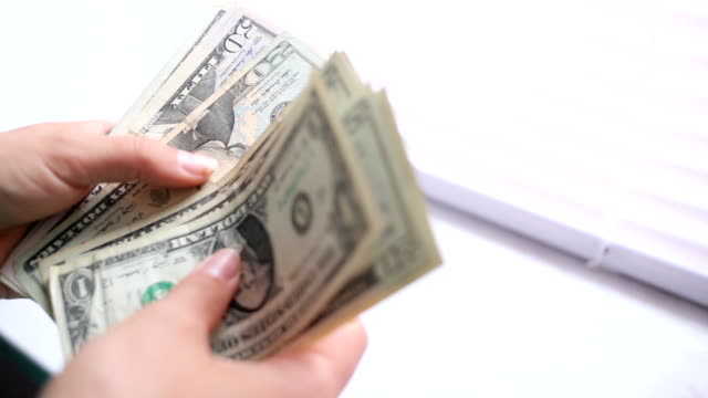 Close-up of a businesswoman's hands counting hundred dollar bills at a table