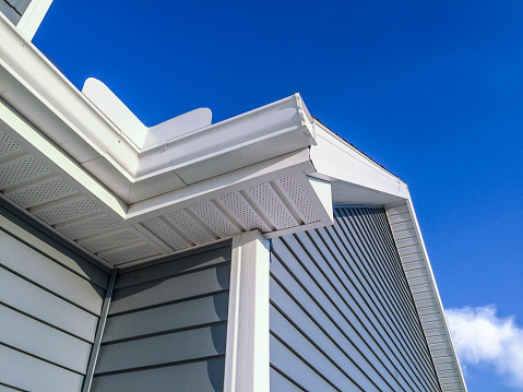 A low angle view of soffit, gutters, downspout and vinyl siding on a new home. Blue sky is in the background.