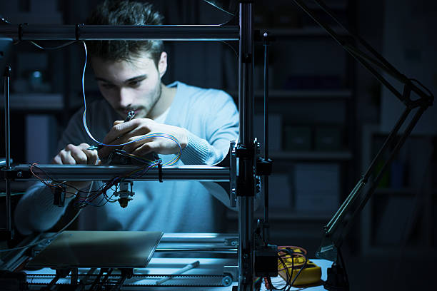 Young engineer working on a 3D printer Young engineer working at night in the lab, he is adjusting a 3D printer's components, technology and engineering concept 3d printing photos stock pictures, royalty-free photos & images