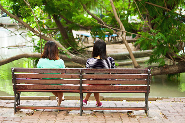 Bangkok, Thailand - June 28, 2016: Two young thai girls sitting on bench of campus Chandrakasem university at mere. In background are trees.