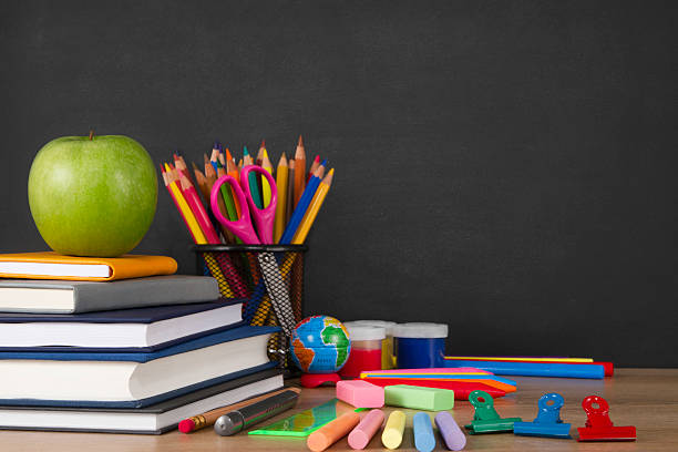 Stack of books and school supplies in front of a black chalkboard