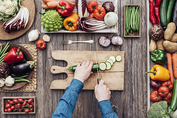 Cooking in a rustic kitchen Man cooking and slicing fresh vegetables on a rustic kitchen worktop, healthy eating concept, flat lay knolling concept stock pictures, royalty-free photos & images