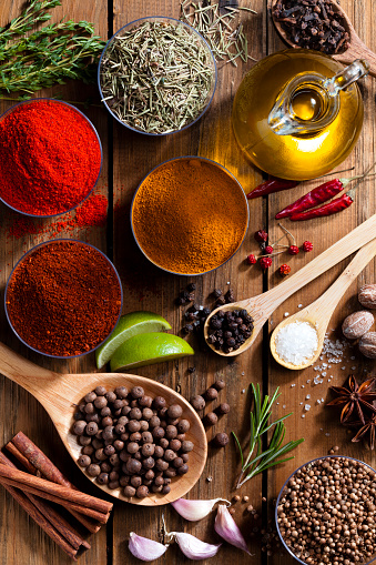 Rustic table filled with a large variety of exotic spices and herbs shot directly from above. The ground spices are in small bowls while the rest of the spices are placed on wood spoons and directly on the rustic wood table. The main light comes from the top-right side giving a nice shadow to the composition. DSRL studio photo taken with DSRL Canon EOS 5D Mk II and Canon EF 100mm f/2.8L Macro IS USM