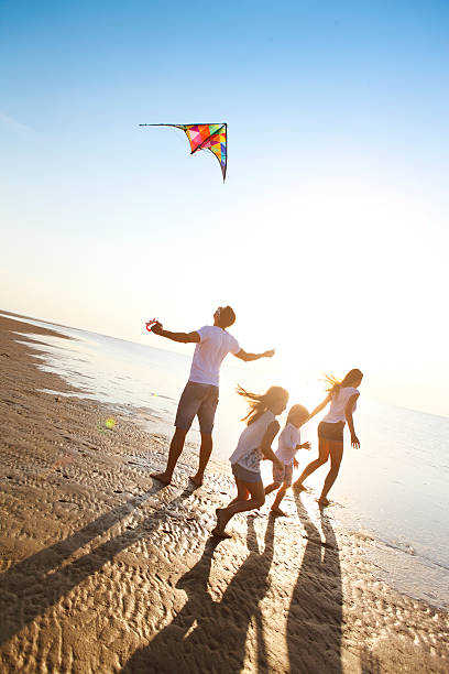 bonne jeune famille avec voler un cerf-volant sur la plage - être aux anges photos et images de collection