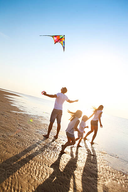 felice giovane famiglia con il volo di un aquilone sulla spiaggia - travel red vacations outdoors foto e immagini stock