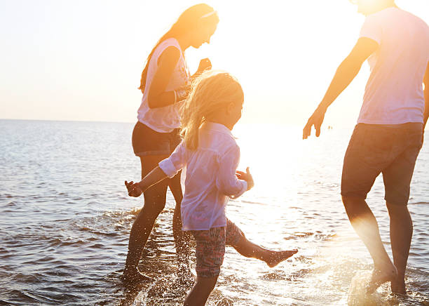 Happy young family having fun running on beach at sunset