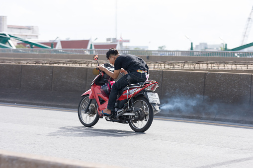 Bangkok, Thailand - June 20, 2015: Unsafe Young man not wearing helmet speeds up a motorbike on the Phra Pok Klao Bridge to cross Chao Phraya River