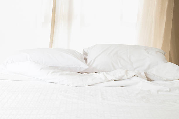 istock Messy white bed with pillow and blanket morning sunlight through 586706236
