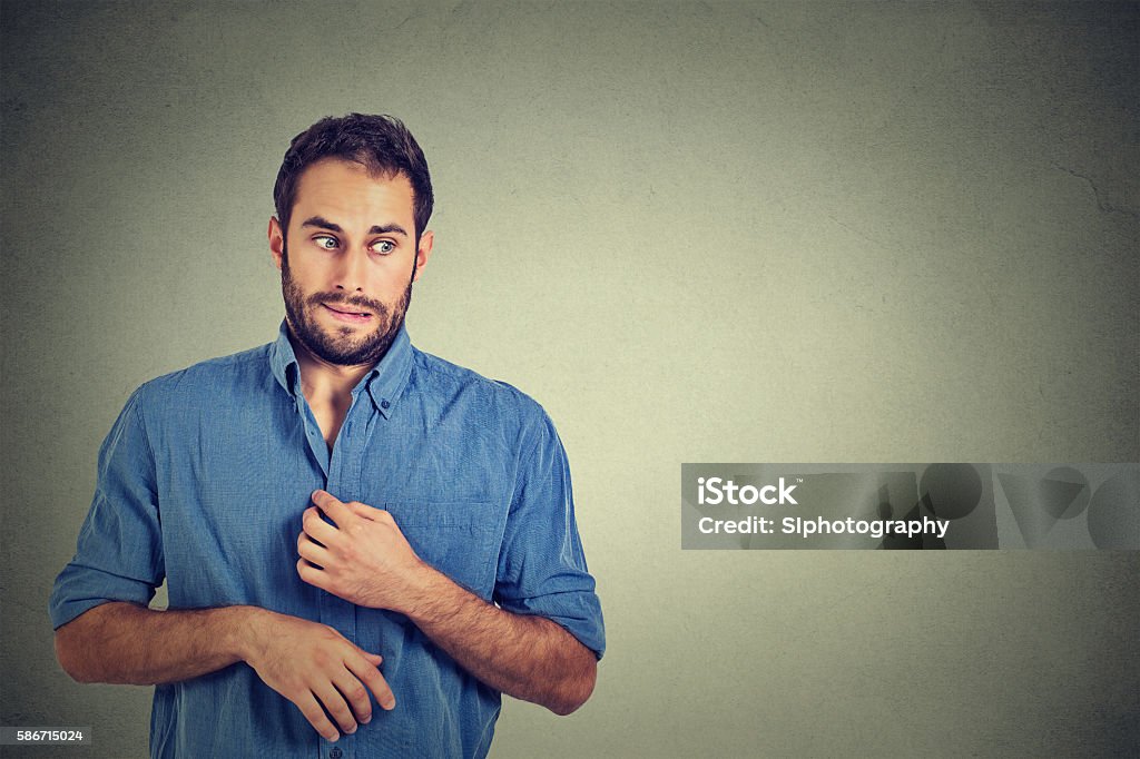 man in awkward situation, playing nervously with hands Portrait young man opening shirt to vent, it's hot, unpleasant, awkward situation, playing nervously with hands. Embarrassment. Isolated gray background. Negative emotions facial expression feeling Men Stock Photo