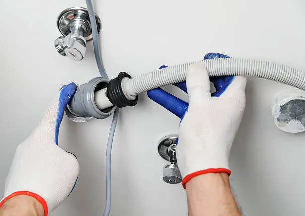 Installation of household appliances. Workman attaches a drain hose to a sewage pipe.