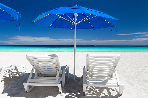 istock Caribbean beach with blue sun umbrellas and white beds 586721276