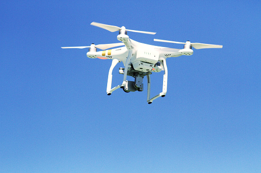 White drone  flying with camera record liens against blue sky
