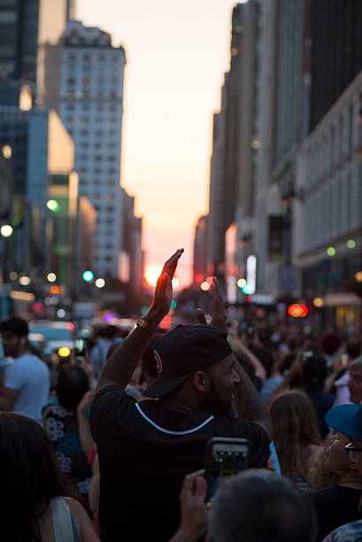 New York City, USA - July 12, 2016: A man stands in a crowd on 34th Street in front of the Macy's Store in Midtown Manhattan, clapping for the Manhattanhenge sunset. Manhattanhenge, also called the Manhattan Solstice, refers to the two or so days each year when the setting sun is aligned with the east–west streets of the main street grid of Manhattan, New York City.