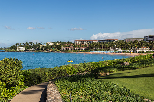 Wailea Beach, Maui, tawny-colored sand is lined by palm trees and a paved walkway connecting the shoreline to the area's hotels, shops and restaurants.