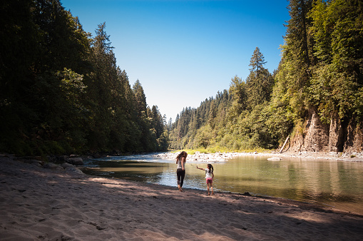 A mother and daughter are playing together along the beautiful banks of the Sandy River in Oregon. The little girl is playfully throwing sand at her mother, as she chases her.