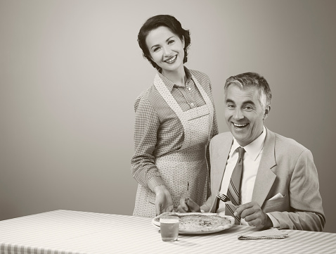 Happy vintage couple having dinner, she is serving a pizza to her husband