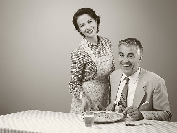 Smiling wife serving dinner Happy vintage couple having dinner, she is serving a pizza to her husband stereotypical housewife stock pictures, royalty-free photos & images