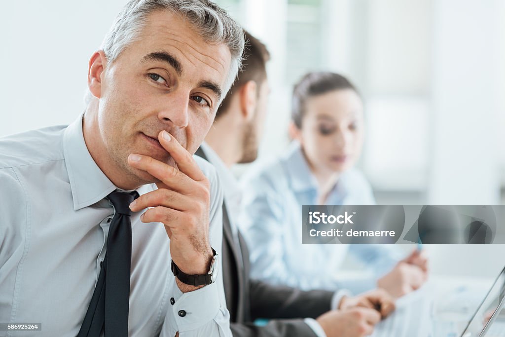 Confident smiling businessman posing Confident professional business man smiling at camera, office and business team working on background, selective focus Adult Stock Photo