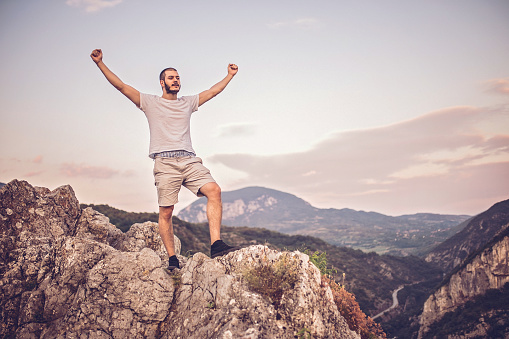 Man standing on a mountain peak with his arms outsreched enjoying the view.