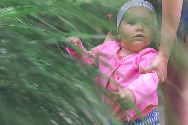 17 months old baby is asking about nature , touching long grass and learning . discovering the world